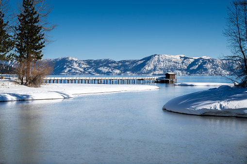 Where the Truckee River meets Lake Tahoe in the Winter, featuring cloudless blue sky and water, and a pier