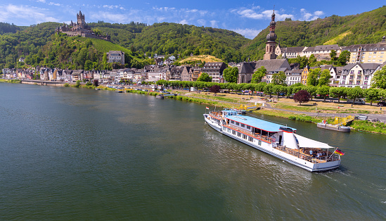 Passenger tourist ship goes along the Moselle River against the backdrop of the city of Cochem on a sunny summer day. Germany