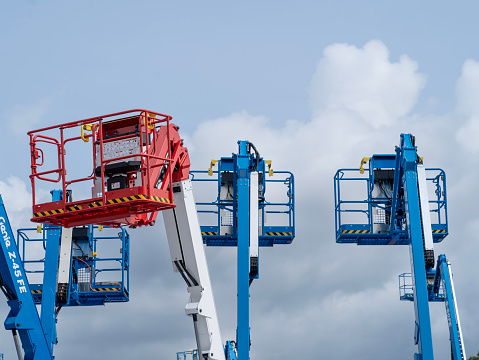 Close-up to a group of different aerial work platforms for construction and material handling stored at the factory. blue, red and white chests