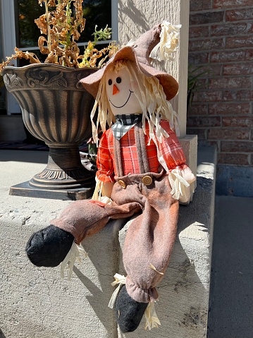 Scarecrow doll sitting on the edge of the front porch