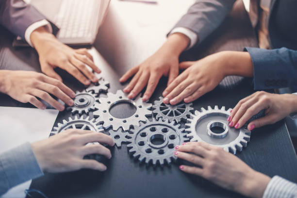istock People joining cog wheel on the black desk. 1653216534