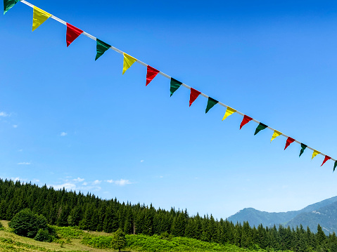 Multicolored garlands or flag flutter in the wind on a summer sunny day on mountain with a blue sky. The concept of festive design of street festivals. Retreat yoga festival.