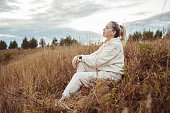 A woman in a tracksuit sits on top of a hill on a summer day and enjoys nature.