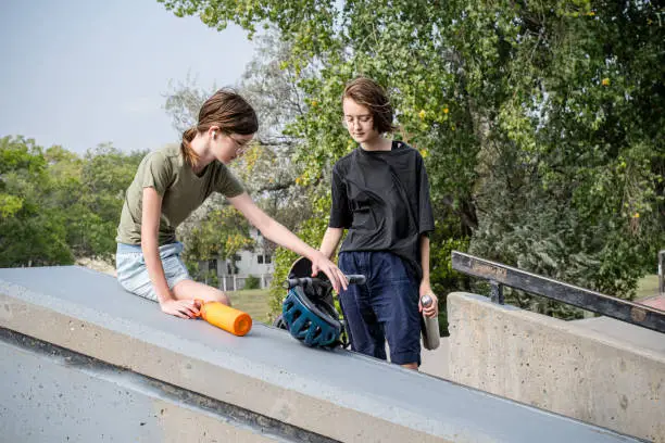 The bond between siblings shines as these adventurous teens stand side by side, helmets on, skateboards and scooters ready, ready to create lasting memories at the skate park