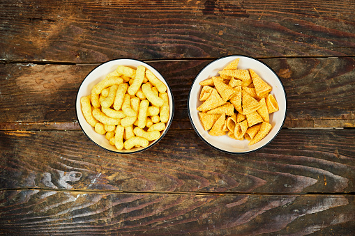 Peanut flips and cone corn chips in a ceramic bowl on wood table . Also known as Bamba, peanut puffs or snips, is a puffed, peanut-flavored corn snack