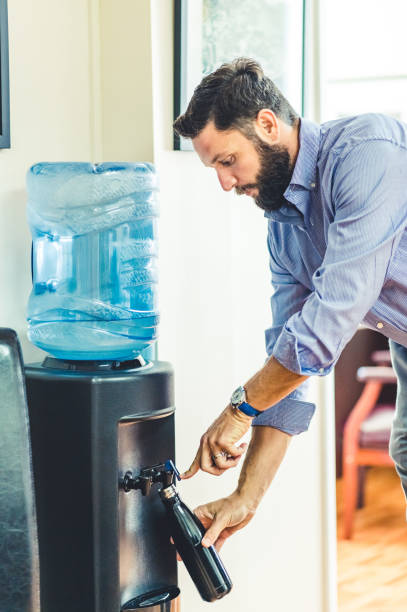 istock Man refills his reusable water bottle at a water cooler in an office 1653311902