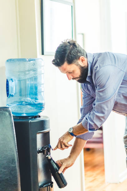 istock Man refills his reusable water bottle at a water cooler in an office 1653313612