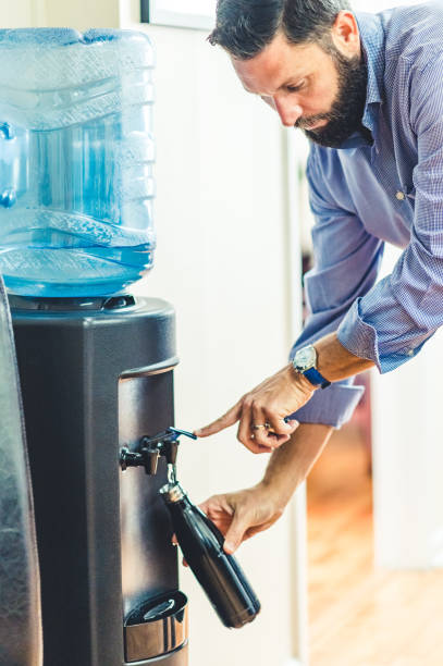 istock Man refills his reusable water bottle at a water cooler in an office 1653315391