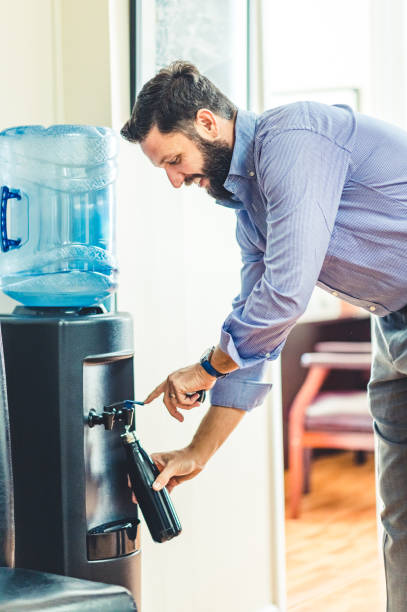 istock Man refills his reusable water bottle at a water cooler in an office 1653315392