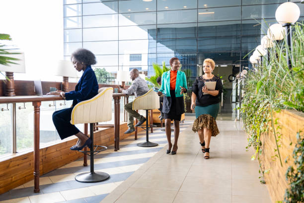 Corporate professionals working in modern office building Nairobi business people aged 20s to 40s sitting independently at window counter space and smiling women approaching camera, walking and talking. east africa stock pictures, royalty-free photos & images