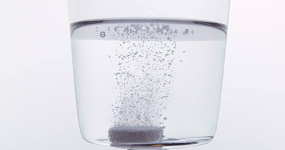Tablets Falling and Dissolving into a Glass of Water against White Background