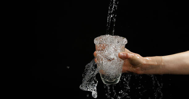 istock Woman's Hands and Water Flowing in Glass on Black Background 1653411488