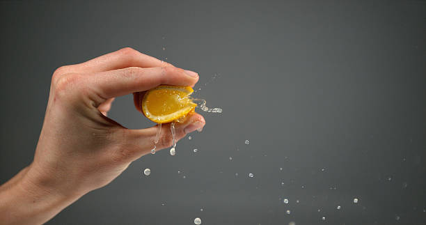 istock Hand of Woman Squeezing Orange against Black Background 1653412113