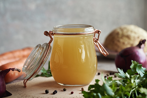 Chicken bone broth in a glass jar with parsley, carrots, onion and celery root