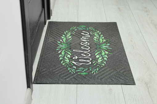 Doormat with word Welcome on white floor near entrance