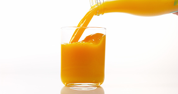 Close-up of slice of orange falling into a glass of juice against white background.