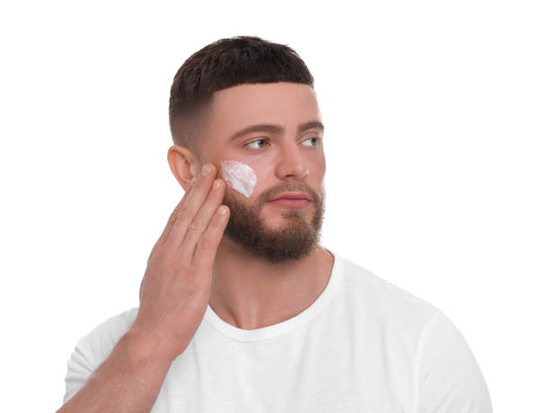 istock Handsome man applying cream onto his face on white background 1653469967