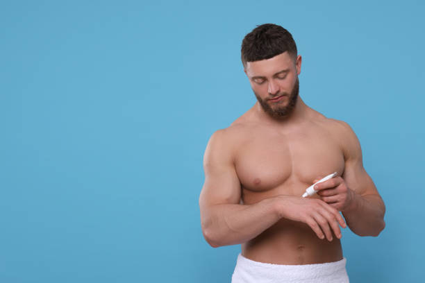 istock Handsome man applying body cream onto his hand on light blue background, space for text 1653469988