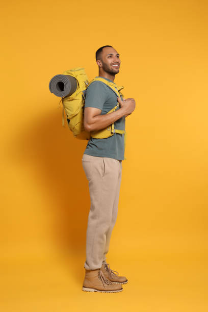 Happy tourist with backpack on yellow background