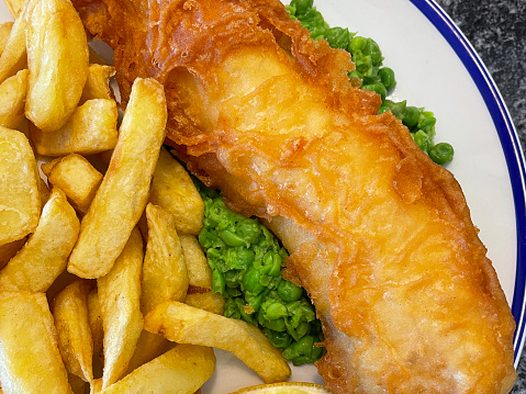 Stock photo showing close-up view of battered cod and chips with mushy peas on a blue rimmed plate.