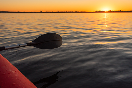 Image of kayak paddles above the dark and calm waters of the Pacific. The sky above Mission Bay is orange and looks like it's on fire, from the magical sunset. San Diego, California