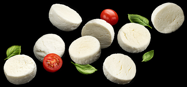 Falling mozzarella cheese slices with tomato and basil leaves isolated on black background, caprese salad ingredients