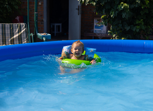 Children swim in the blue pool on a hot summer sunny day. Children have fun swimming in the cool water of the pool. In the summer, in the backyard of the house, children bathe and splash in the pool..