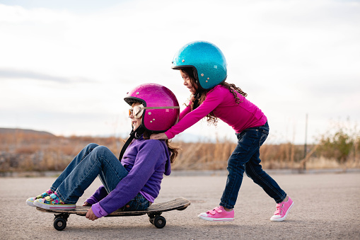 Two girls are having fun on a skateboard. One pushes the other while they have fun together.