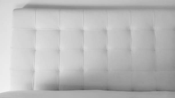 Soft headboard. Upholstery for furniture made of genuine or artificial leather and quilted fabric. Soft headboard against a light wall. Black and white monochrome photo Soft headboard. Upholstery for furniture made of genuine or artificial leather and quilted fabric. Soft headboard against a light wall. Black and white monochrome photo. leather cushion stock pictures, royalty-free photos & images