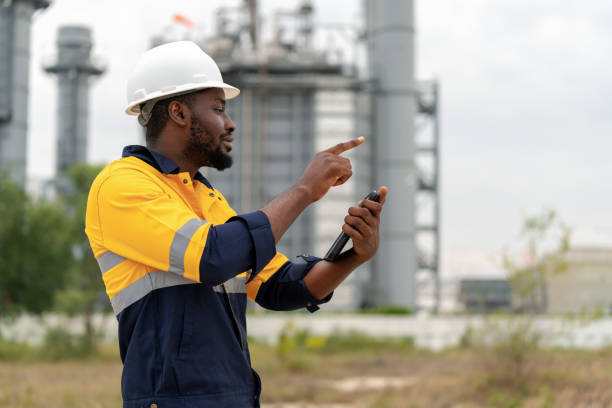 African American engineer at the forefront of enhancing power plant efficiency. The engineer stands confidently at a power plant generator, intently using a laptop to analyze crucial data. Contributes significantly to driving growth and innovation. African American engineer at the forefront of enhancing power plant efficiency. The engineer stands confidently at a power plant generator, intently using a laptop to analyze crucial data. Contributes significantly to driving growth and innovation within the energy sector. project manager remote stock pictures, royalty-free photos & images