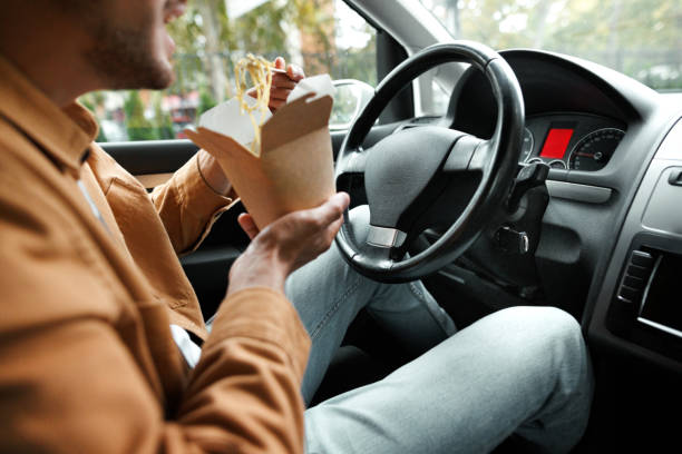 istock Young casually clothed man eating while driving car in the city 1653821849