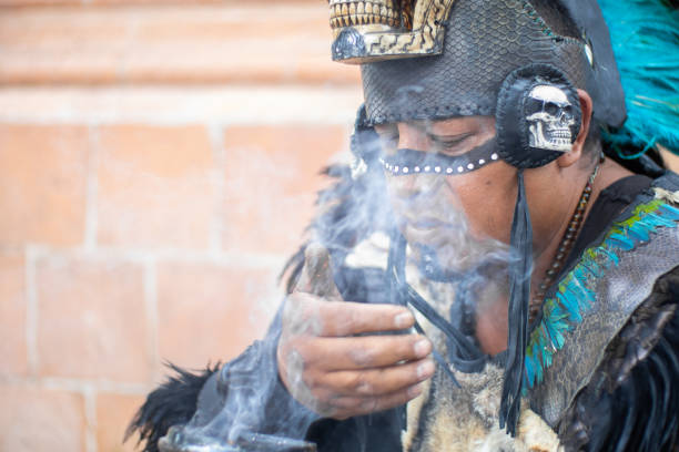 gros plan d’un chaman concentré sentant la fumée d’un calice ou d’un calice rituel, danseur aztèque avec coiffe à plumes et crânes sur son costume, artiste traditionnel mexicain de culture hispanique - asian tribal culture photos photos et images de collection