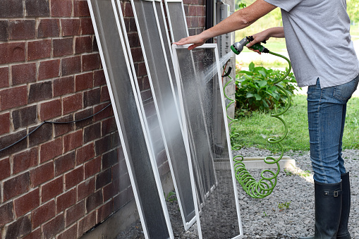 Woman washing window screens with water hose outdoors
