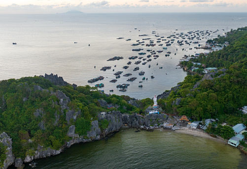 Island landscape with blue sea and giant Guan Yin Buddha statue, in the distance is a cobia farming village of fishermen on the island, Kien Giang province