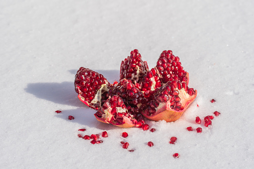 Open pomegranate fruit with red seeds on a white snow in winter, close up. Organic bio fruits
