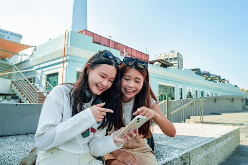 Candid shot of teenage girl and female friend looking at smart phone that make them laughing