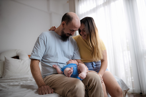 Young parents sitting on the bed and enjoying a tranquil moment with their 8-week old baby boy