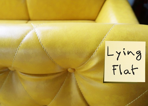 Yellow sofa with stick note written LYING FLAT, means movement of young people in China taking a break from relentless work, rejection of societal pressures to overwork