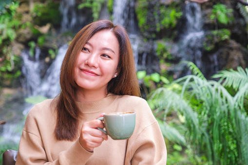 Smiling young woman holding and smelling coffee to go in coffee shop