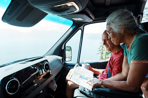 A vibrant multiracial senior couple who is on a road trip in their camper van stop on the side of the road to look at a map.