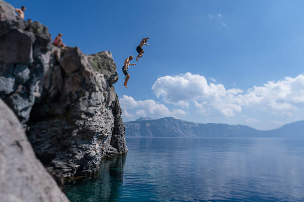 istock Adventurous man and father jumping off cliff into mountain lake 1654167975