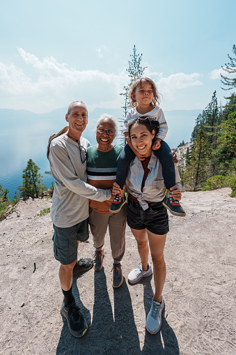 An Eurasian woman holds her three year old daughter on her shoulder and poses with her parents while on a hike near Crater Lake in Oregon during a fun and adventurous summer family camping trip.