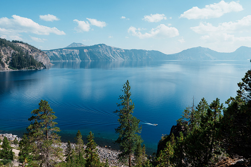 A tour boat races across the calm surface of Crater Lake in Oregon on a beautiful and sunny summer day.
