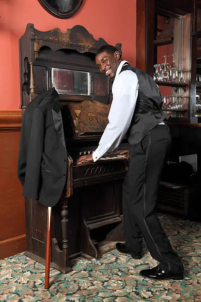 african american, male plays piano organ in bar, bar and glasses in background. 