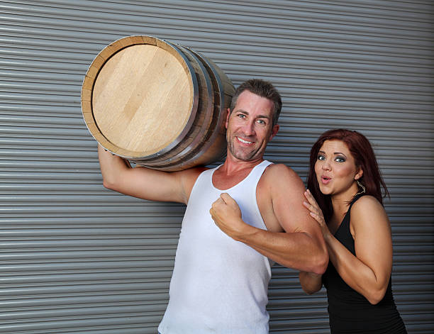 strong caucasian man carries beer barrel admired by girl strong caucasian man carrying beer barrel admired by girl - in front of rolling shutter admired stock pictures, royalty-free photos & images
