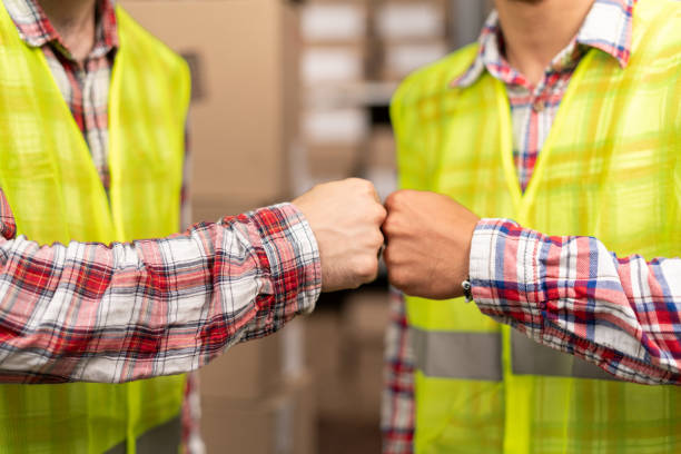 manual worker and businessman fists beat and making deal at warehouse. wholesale, logistic, people and export concept - manual worker handshake industry warehouse imagens e fotografias de stock