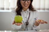 Closeup shot of an unidentifiable doctor holding an apple and a variety of pills in her hands