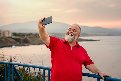 Smiling mature man taking a selfie while on a summer vacation to the sea