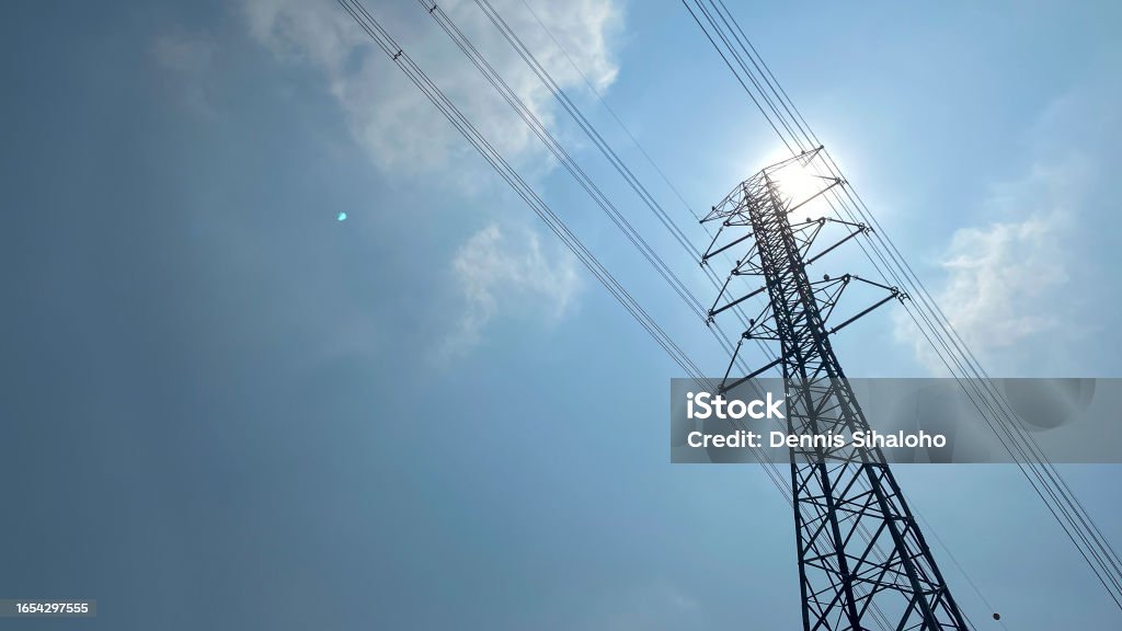 High voltage post, High voltage tower with blue sky background High voltage post. High voltage tower against cloudy blue sky and sun. high-voltage power lines at afternoon with hot sun, high voltage electric transmission tower Air Pollution Stock Photo