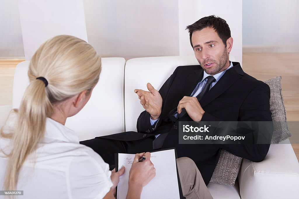 Man talking to his psychiatrist Over the shoulder view of a business man reclining comfortably on a couch talking to his psychiatrist explaining something Above Stock Photo
